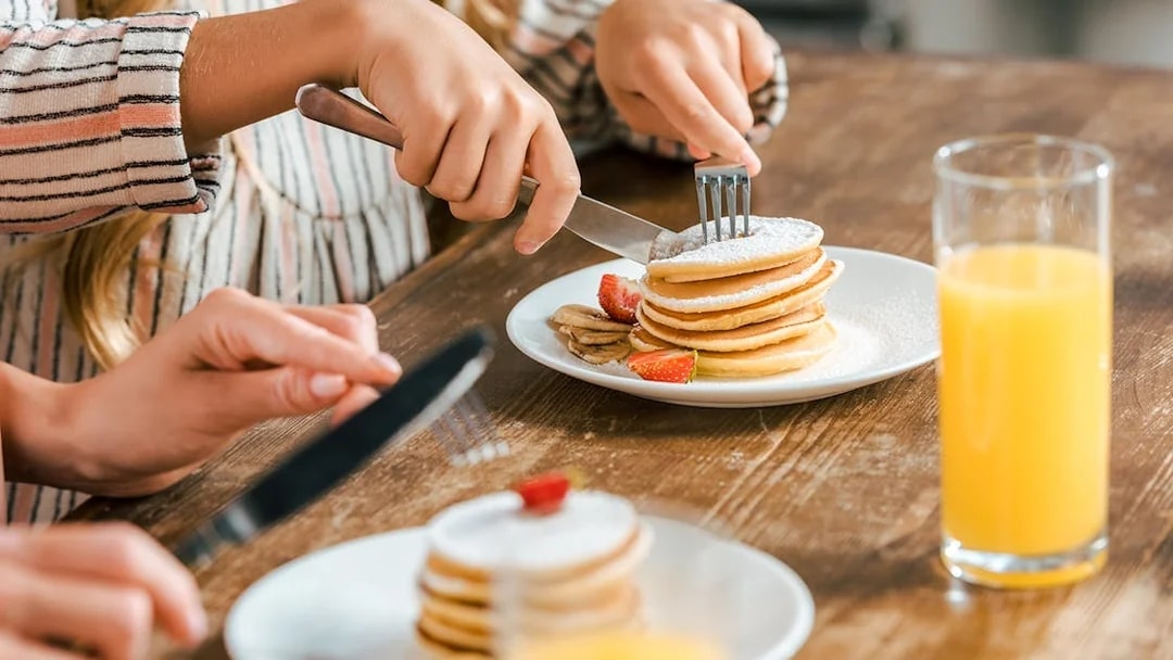 Pancakes with strawberries and bananas on a plate, close up with orange juice.