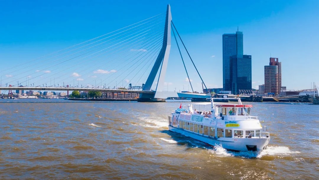 River cruise boat on the Nieuwe Maas with Erasmus Bridge in Rotterdam.