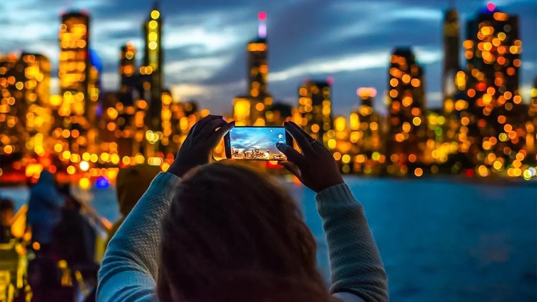 Person photographing Chicago skyline during Lake Michigan sunset cruise.