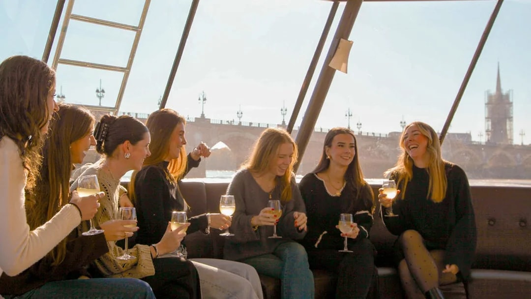 Group enjoying wine on a Bordeaux river cruise with cityscape in background.
