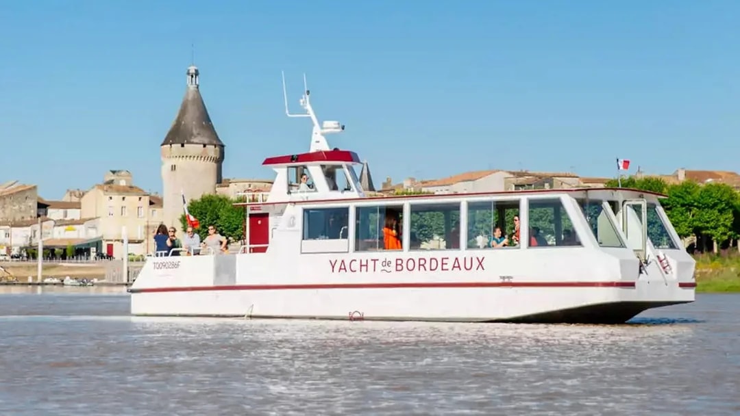 Cruise boat on Bordeaux river with historic tower in background.