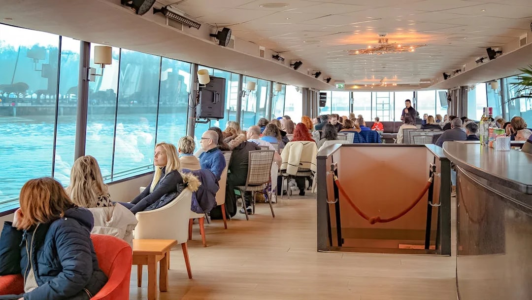 People enjoying a scenic Bordeaux river cruise inside a boat with large windows.