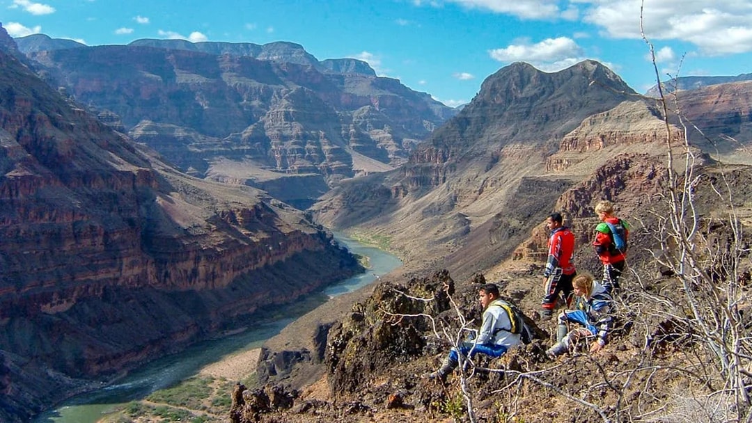 Tourists sitting and standing on a rocky ledge overlooking the Grand Canyon.