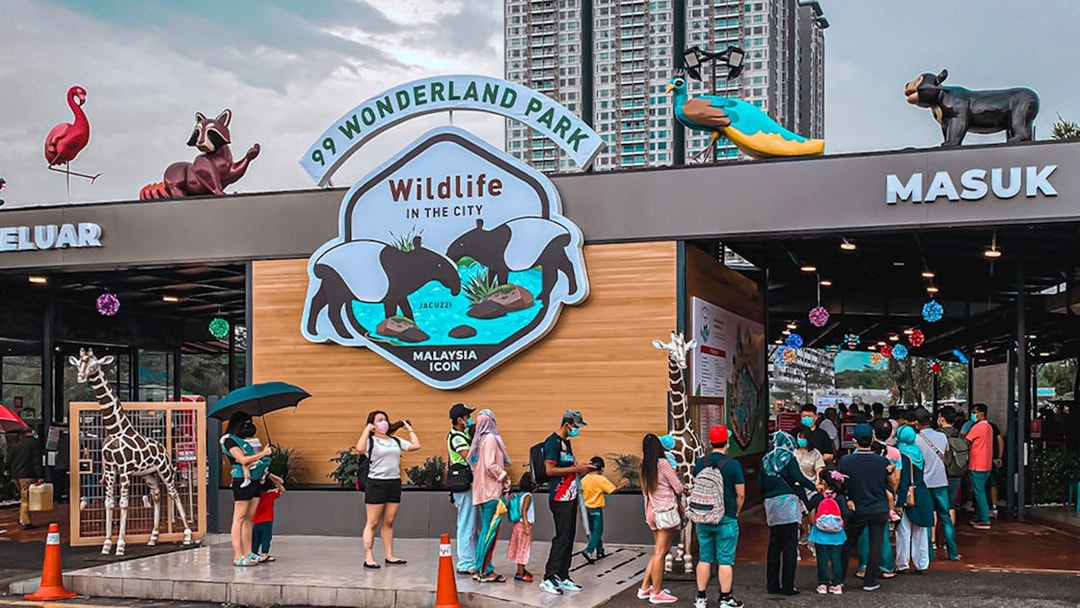 Visitors queue at the entrance of 99 Wonderland Park, Kuala Lumpur, with animal sculptures above.