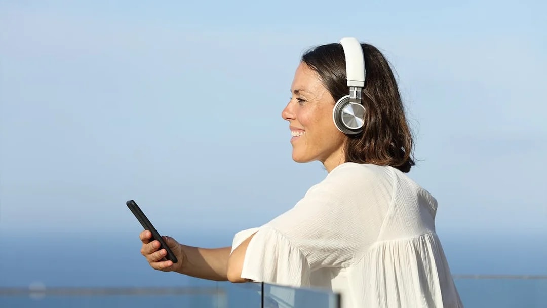 Woman listening to audio guide on ship with earphones, holding smartphone.
