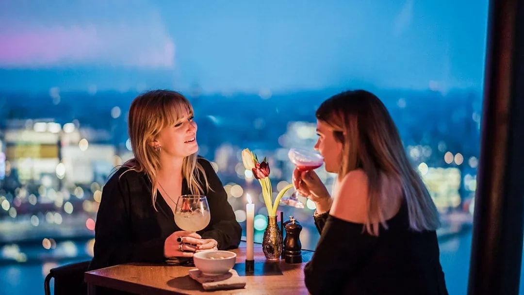 Two people enjoying drinks at a table with a city view at ADAM Lookout, Amsterdam.