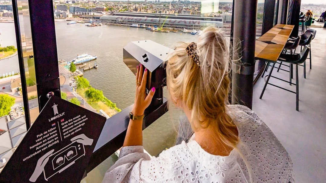 Person using a viewer at ADAM Lookout indoor panorama deck, overlooking Amsterdam.