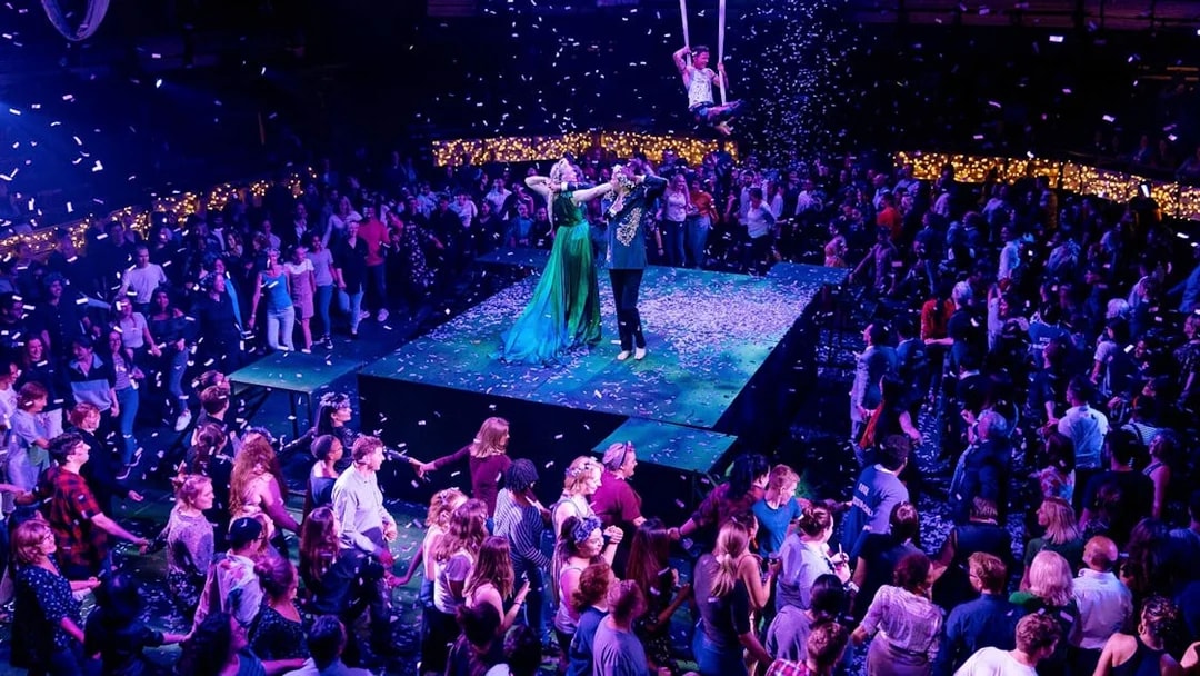 Performers on stage during "A Midsummer Night's Dream" at a seated venue, surrounded by audience.