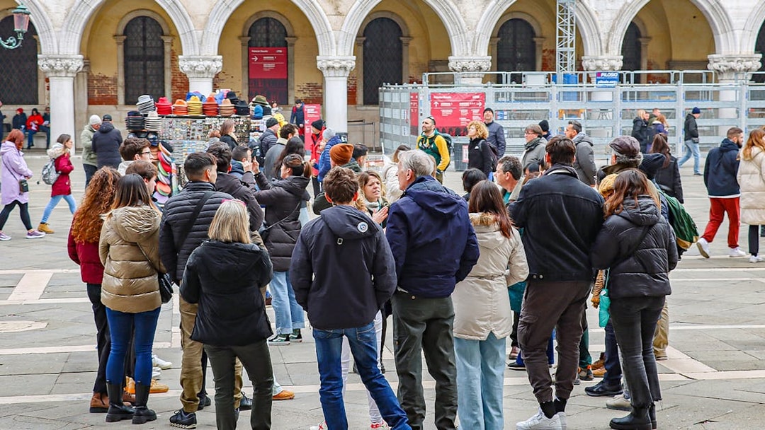 Tour group gathered in a Venetian square, listening to a guide near historic arches.