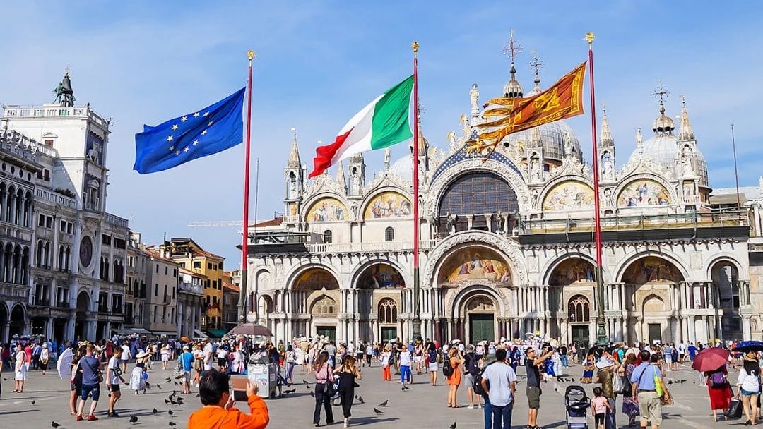 Crowd in front of St Mark's Basilica, Venice, with flags of Italy and EU.