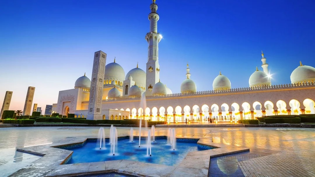 Sheikh Zayed Grand Mosque at dusk, Abu Dhabi, with illuminated arches and fountains.
