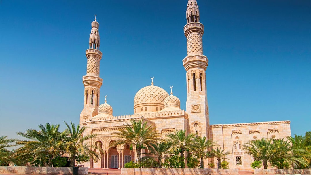 Jumeirah Mosque in Dubai with palm trees and clear blue sky.