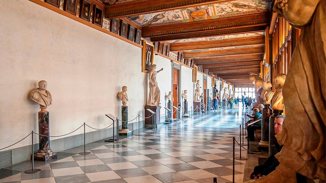 Uffizi Gallery corridor with classical sculptures and visitors in Florence, Italy.