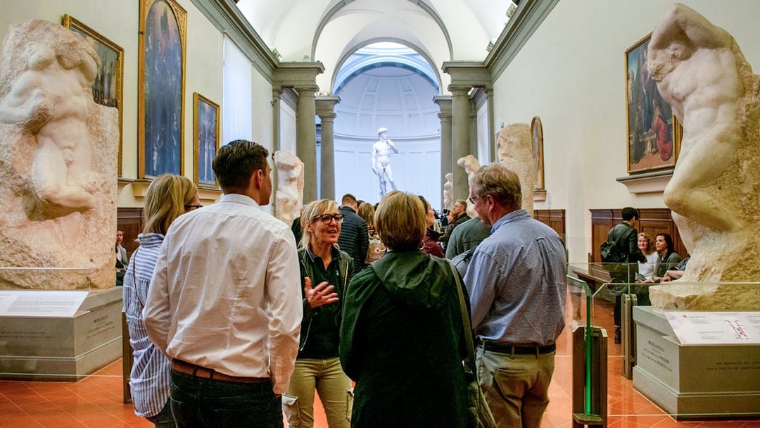 Guide leading tourists through Gallerie dell'Accademia, Florence, with sculptures in view.