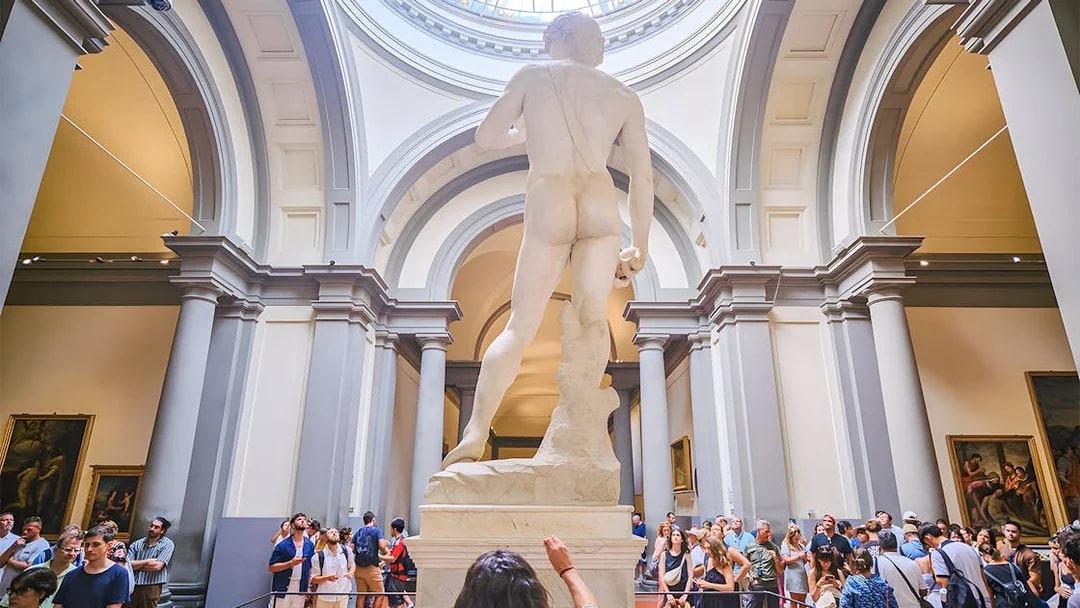 David statue's back view in Accademia Gallery, Florence, with visitors observing.