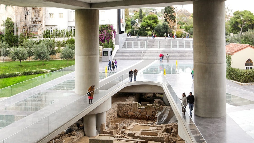 Visitors walking on a glass floor above ancient ruins at the Athens Acropolis Museum.