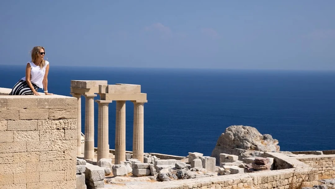 Visitor at the Acropolis of Lindos with ancient columns and sea view in Rhodes, Greece.