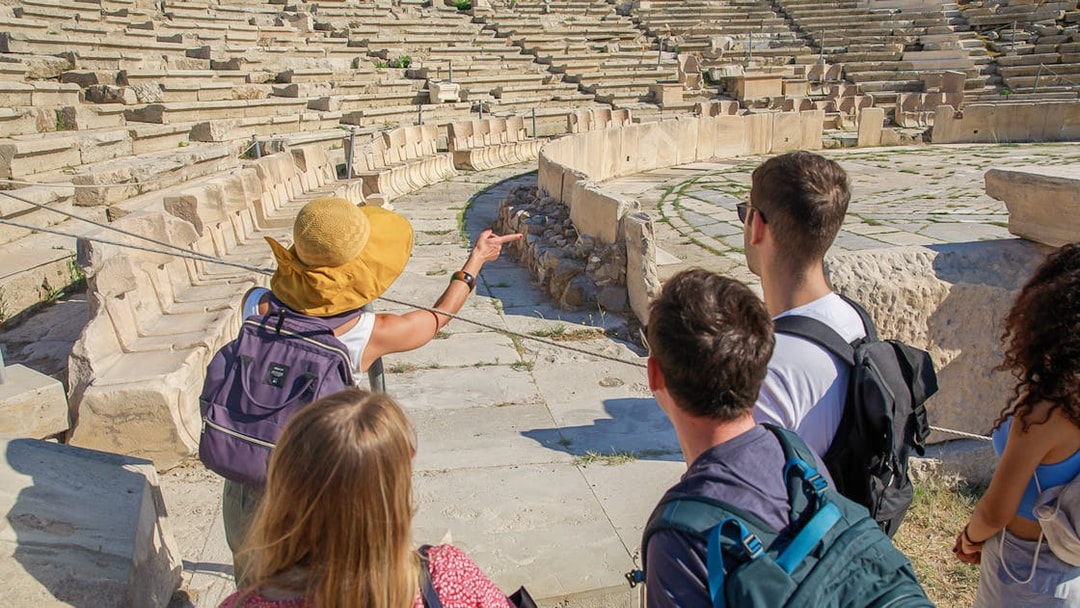 Tour group exploring ancient amphitheater at Acropolis, Athens.