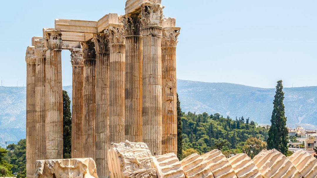 Ruins of the Temple of Olympian Zeus in Athens with mountains in the background.