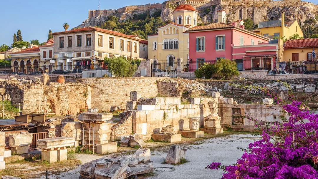Ancient ruins with colorful buildings and Acropolis of Athens in the background.