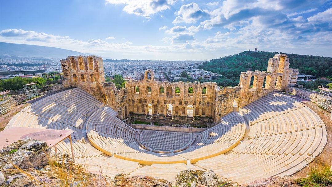 Ancient amphitheater in Athens with cityscape and hills in the background.