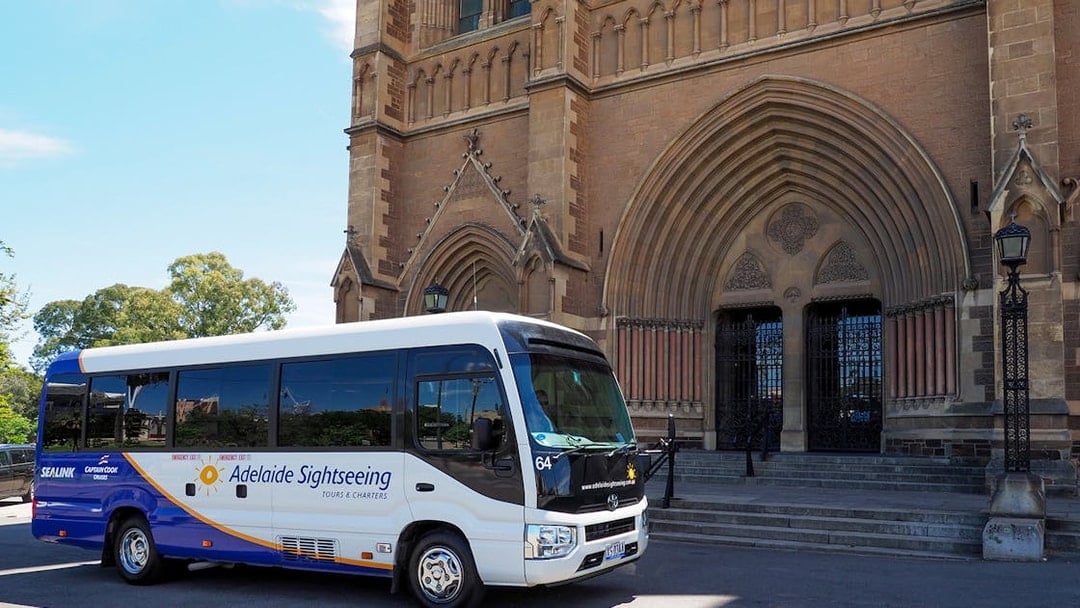 Adelaide sightseeing bus in front of historic cathedral entrance.