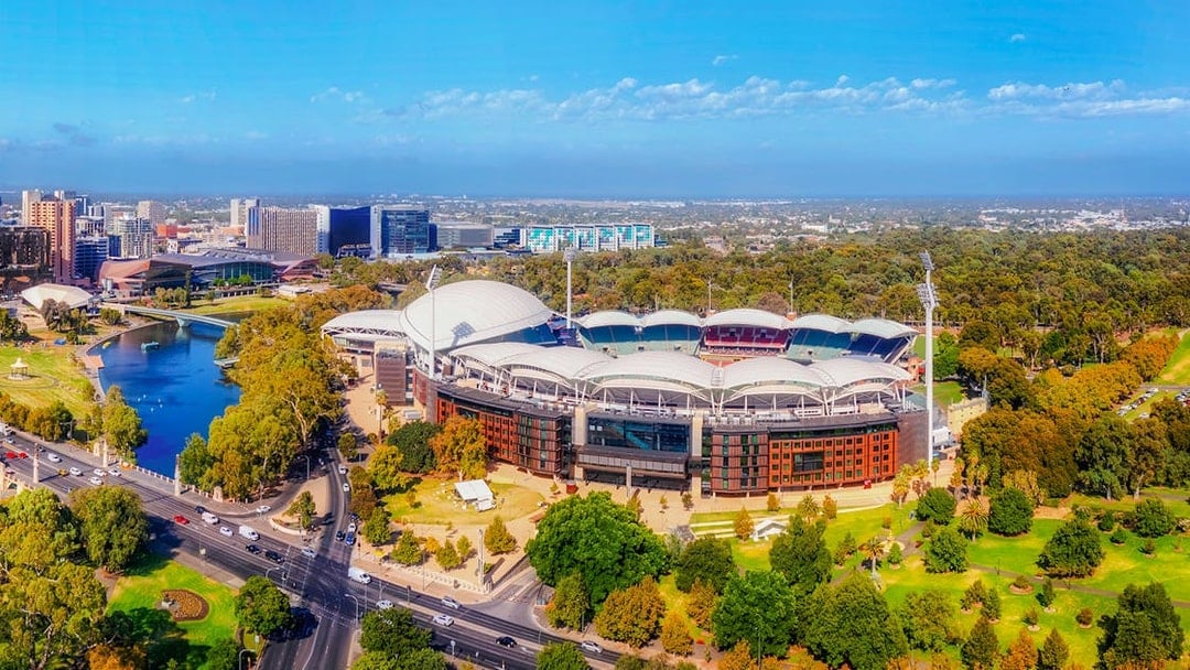 Aerial view of Adelaide Oval Stadium surrounded by parkland and cityscape.