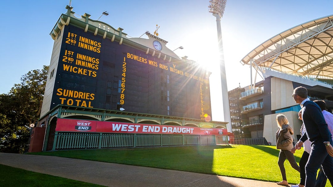 People walking past the historic scoreboard at Adelaide Oval Stadium.
