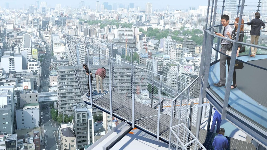 Visitors on Tsutenkaku Tower's observation deck overlooking Osaka cityscape.