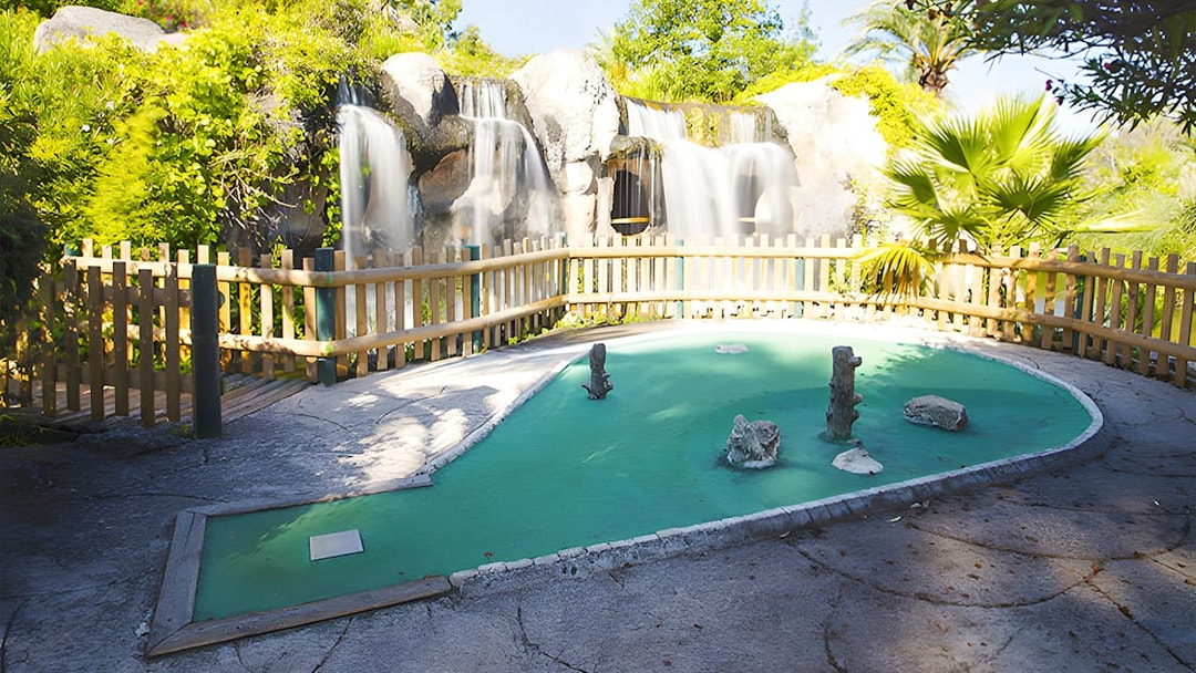 Mini-golf course with waterfall and wooden fence in a lush garden setting.