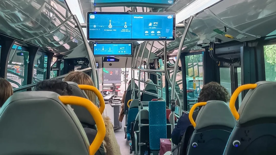 Barcelona Aerobus interior with passengers seated and digital screens displaying route information.