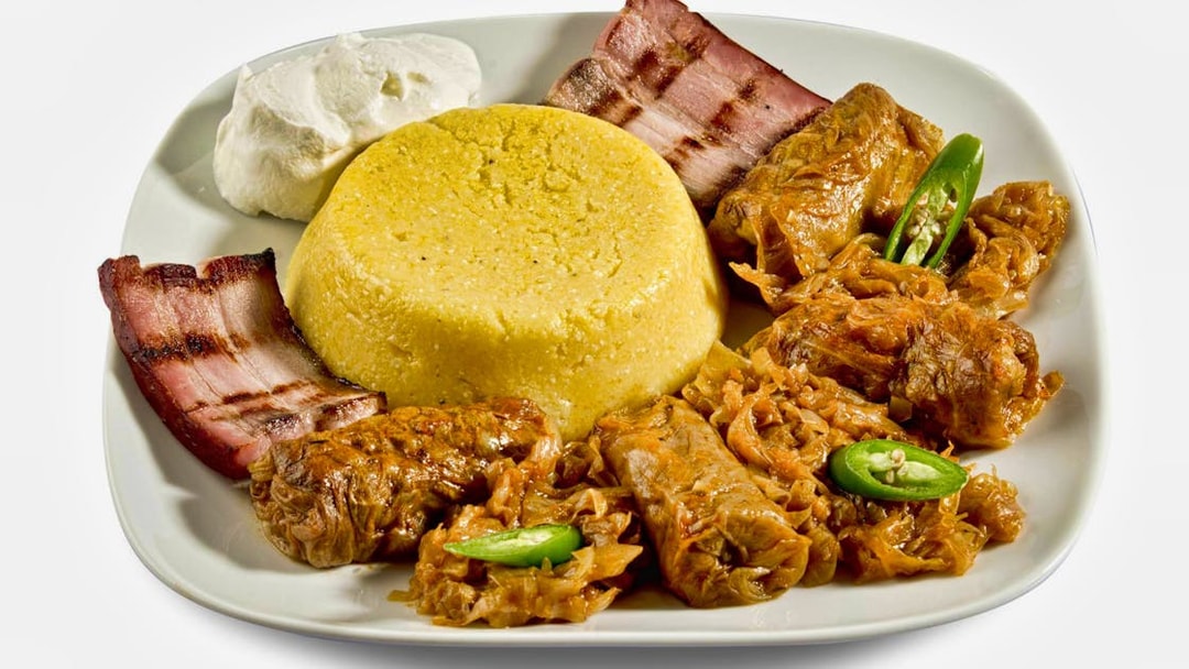 Traditional Romanian meal with polenta, cabbage rolls, bacon, and sour cream.