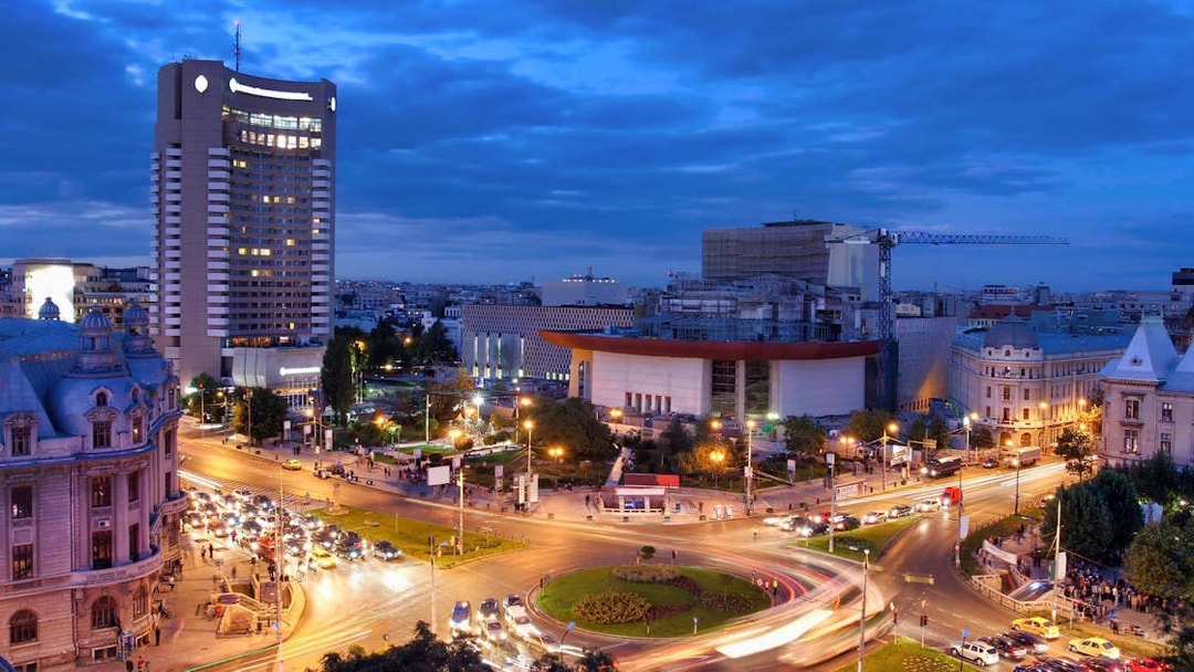 Cityscape of Bucharest at night with illuminated buildings and busy roundabout.