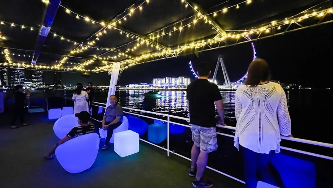 Houseboat deck with people enjoying night view of Ain Dubai Ferris wheel.