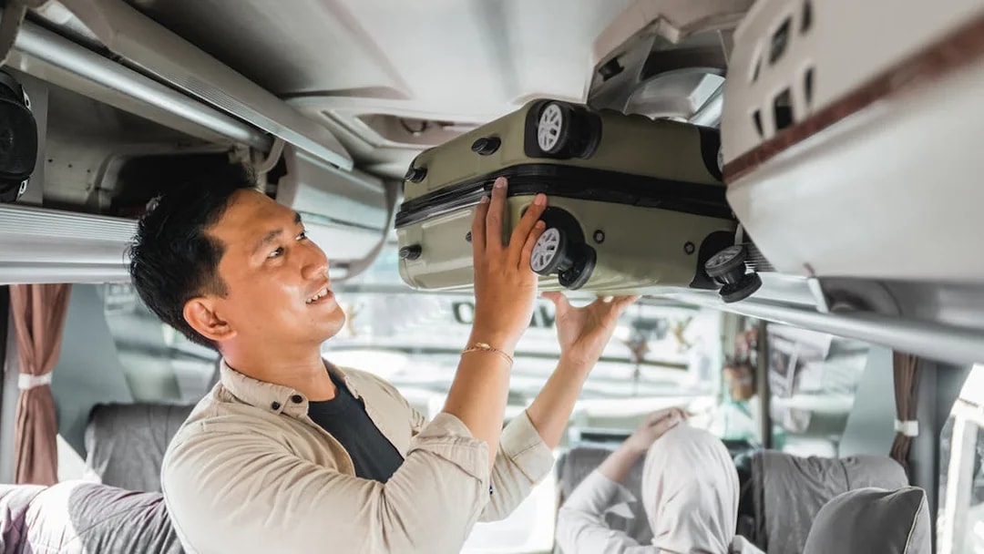 Man placing suitcase in overhead compartment on a bus.