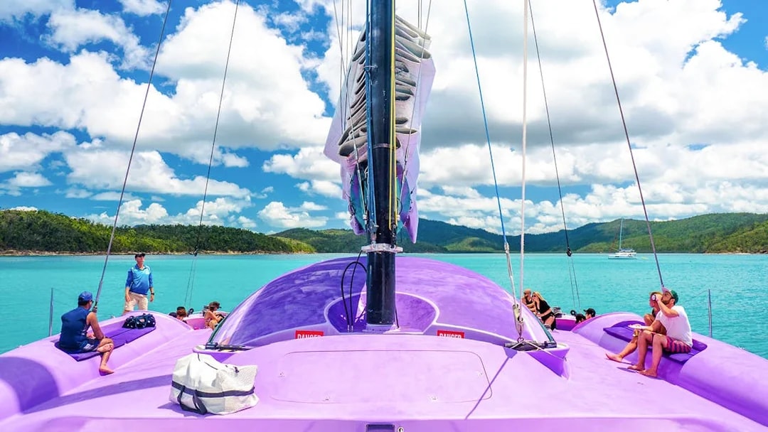 Sailing on a purple catamaran in Airlie Beach with passengers enjoying the view.