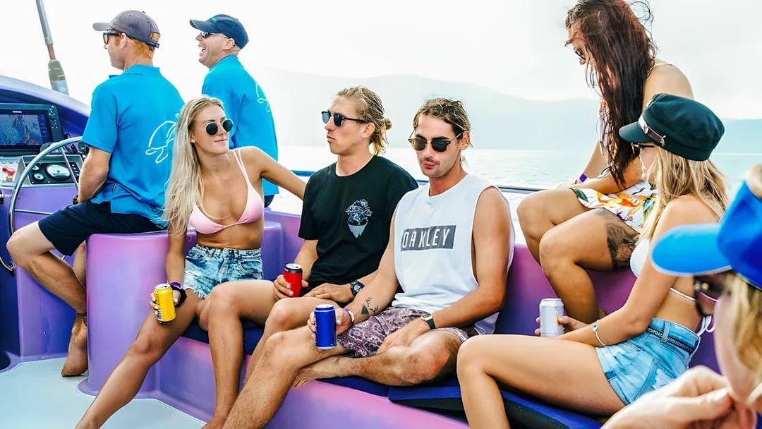 Group enjoying a sailing adventure on a boat at Airlie Beach, holding drinks and relaxing.