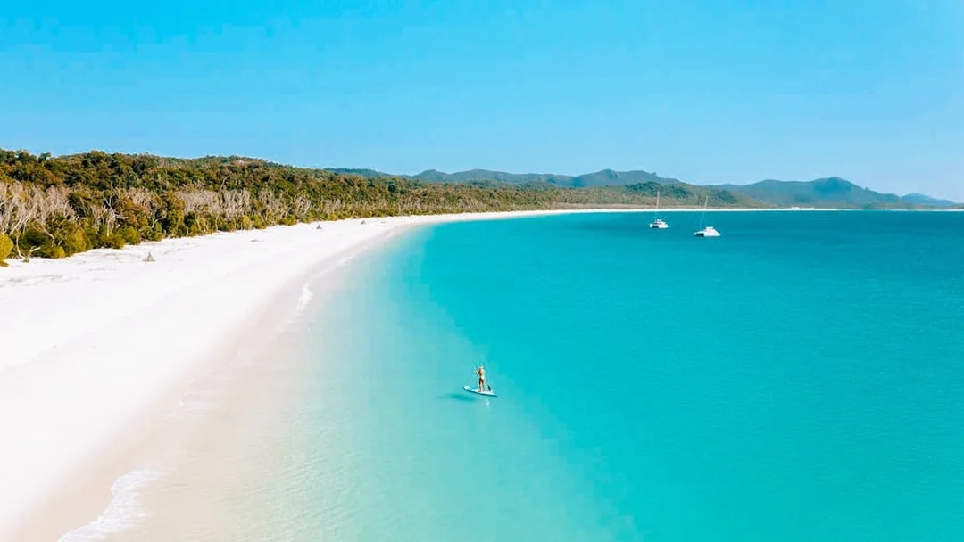 Paddleboarder on turquoise waters near Whitsundays Islands beach.