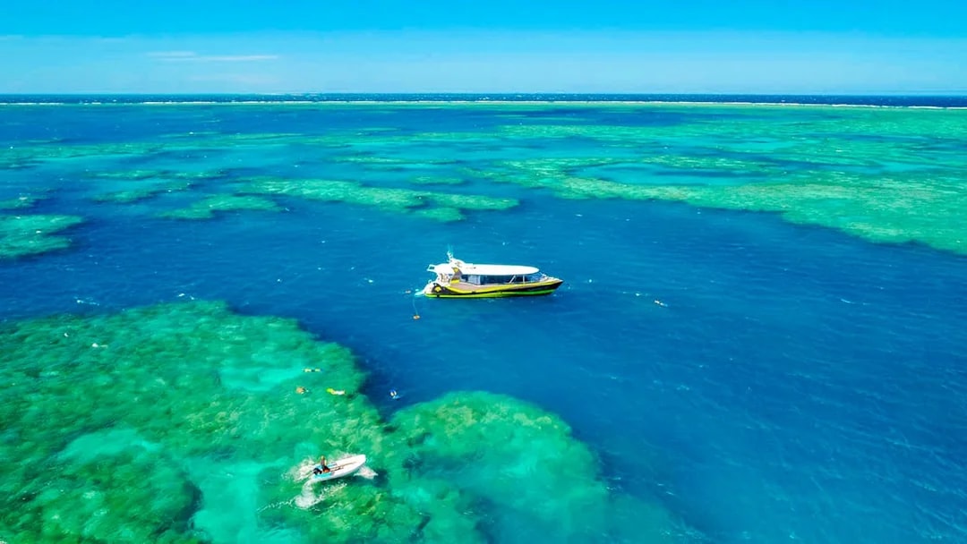 Boat sailing over clear waters of Whitsundays Islands with snorkelers exploring the reef.
