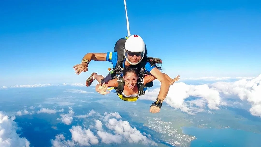 Tandem skydivers over Airlie Beach coastline with ocean and landscape below.