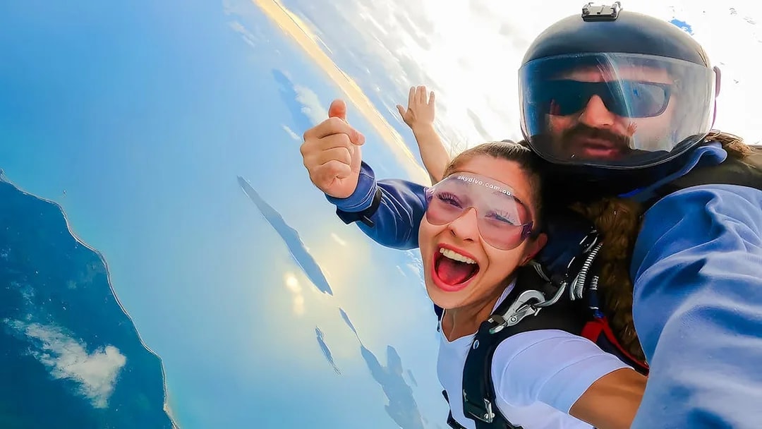 Tandem skydivers over Airlie Beach with ocean and Whitsunday Islands below.