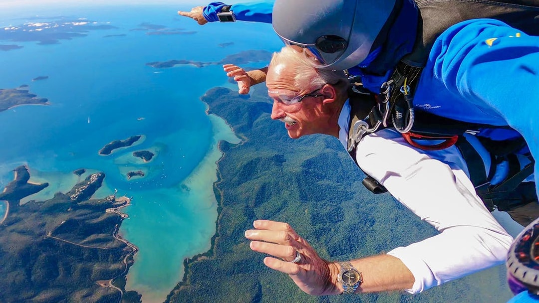 Tandem skydiving over Airlie Beach coastline, Queensland, with vibrant ocean and lush landscape below.
