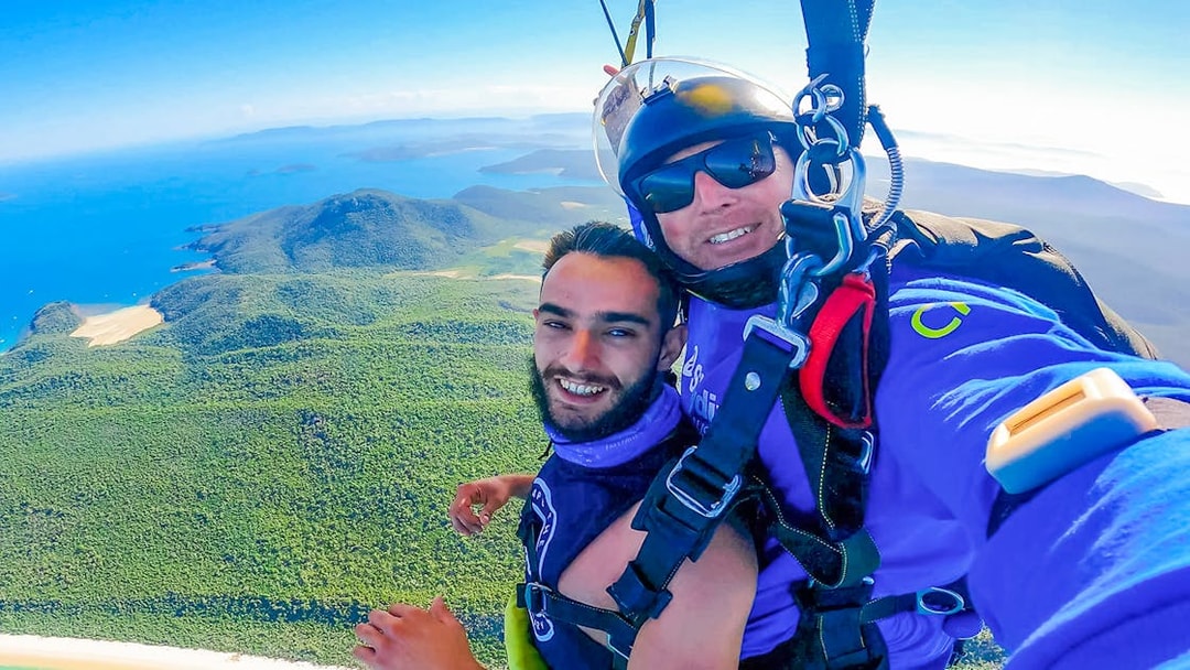 Tandem skydivers over Airlie Beach, showcasing turquoise waters and lush landscape below.