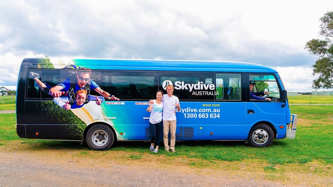 Skydive Airlie Beach bus with skydiving graphic and two people standing beside it.