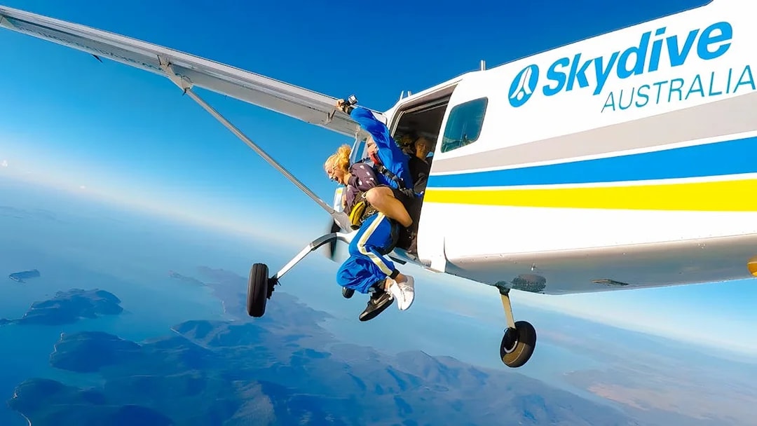 Tandem skydiving over Airlie Beach, instructor and skydiver exiting plane.