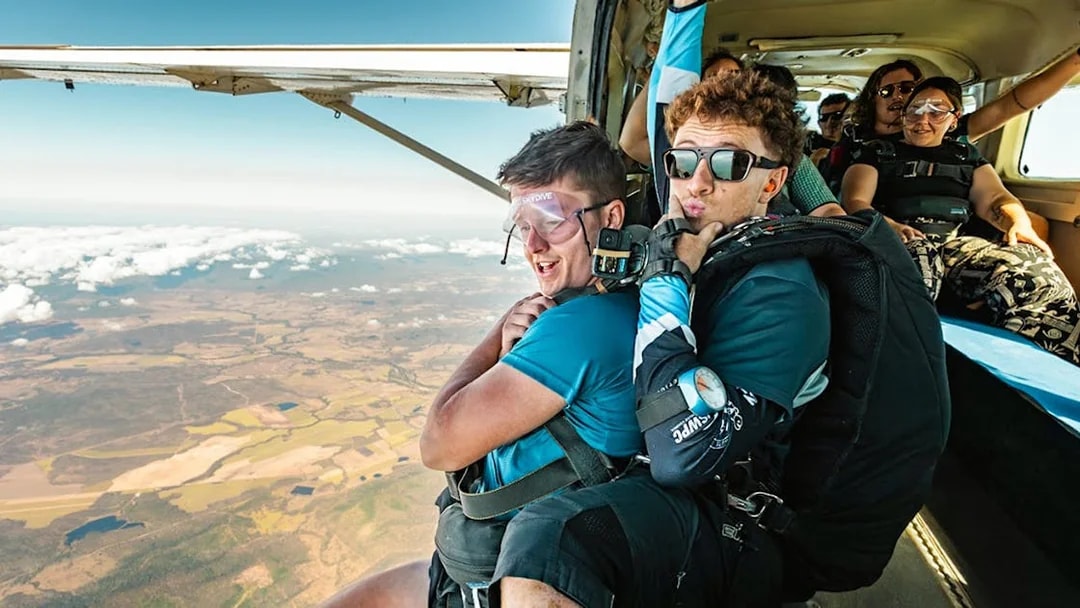 Tandem skydivers preparing to jump over Airlie Beach with scenic landscape below.