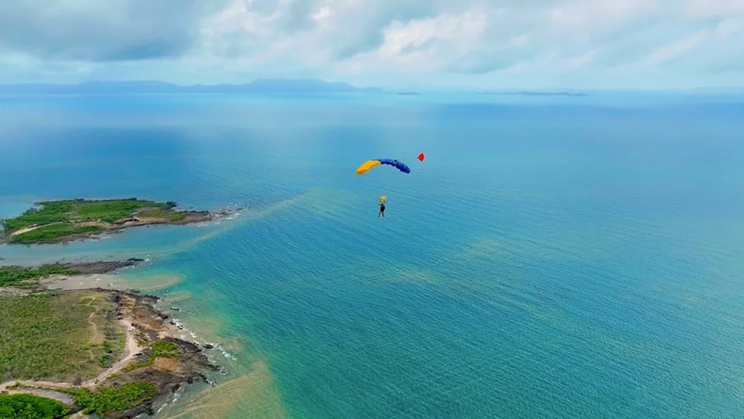 Skydiver descending over ocean near Airlie Beach with parachute.