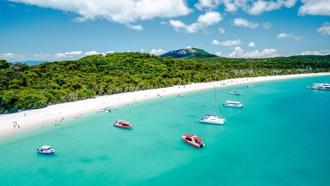 Aerial view of boats near Whitehaven Beach, Whitsundays, with lush greenery and clear blue water.
