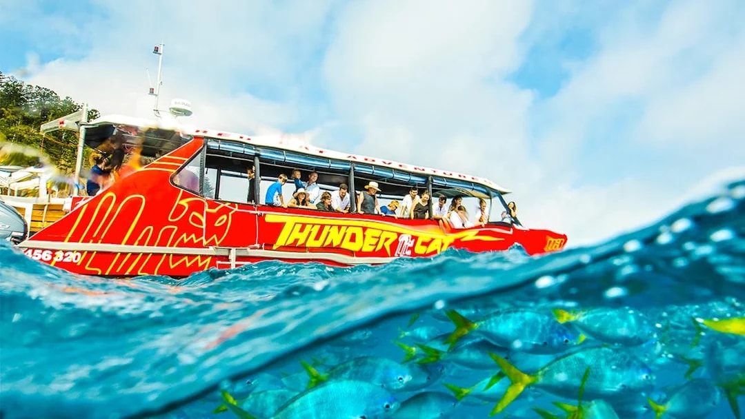 Thundercat boat on Whitsundays tour with tourists, vibrant fish visible underwater.