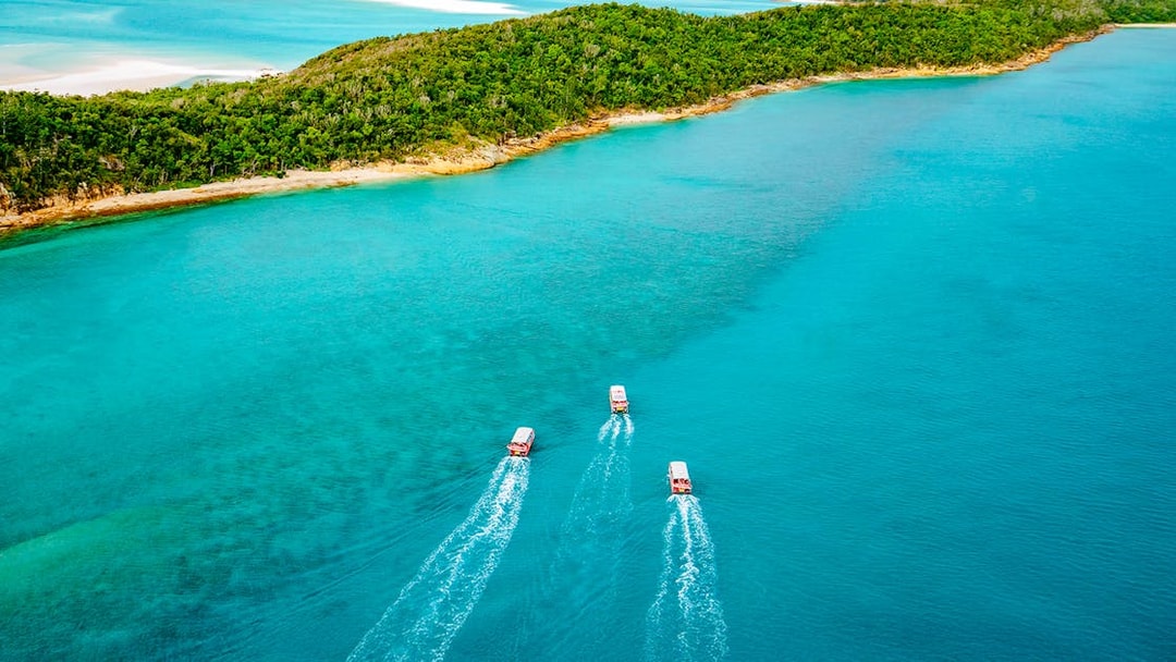 Three boats cruising in turquoise waters near lush Whitsunday Islands on Thundercat Full Day Tour.